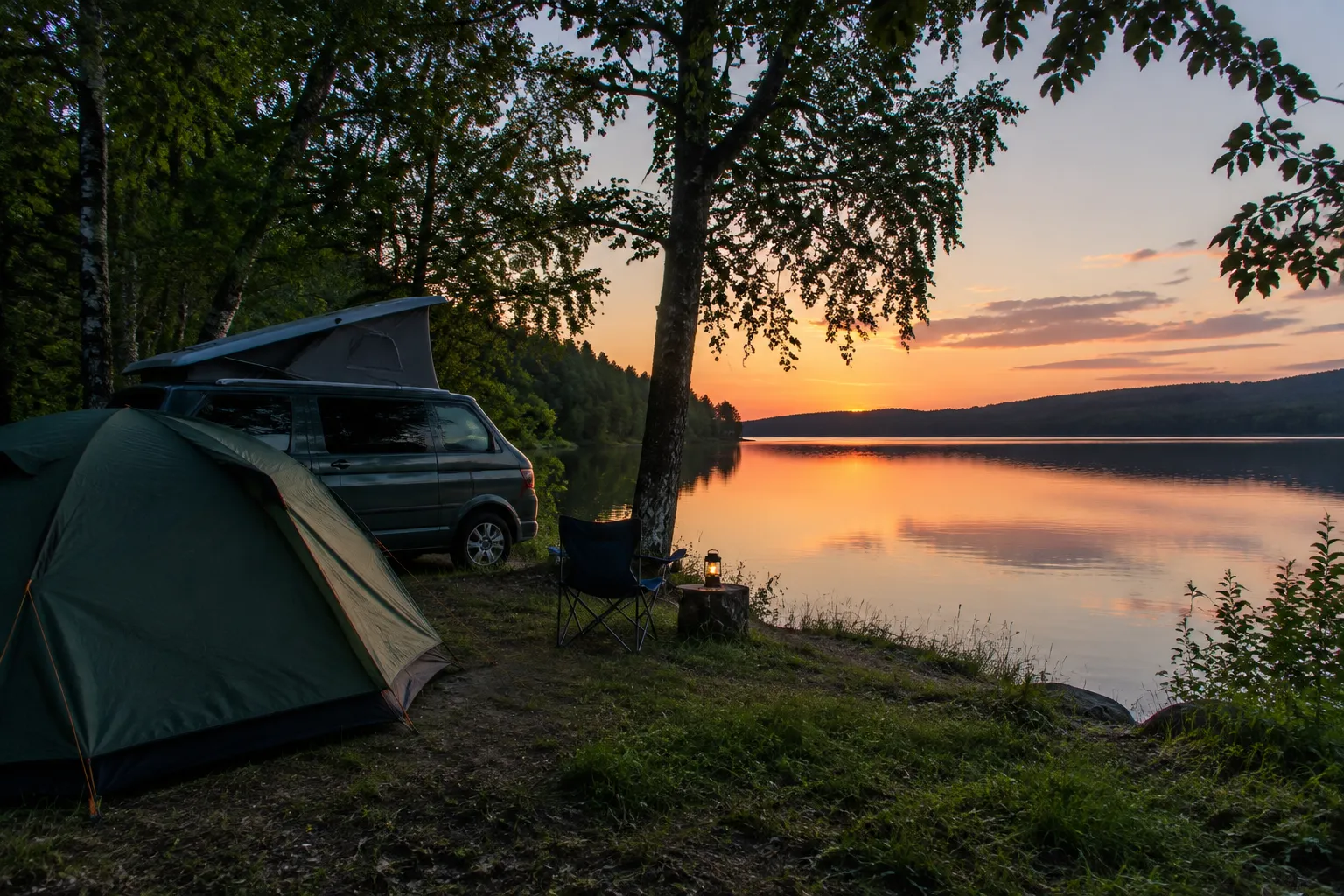 Zelt und Campingbus am Seeufer in der Abenddämmerung mit Stuhl und Laterne